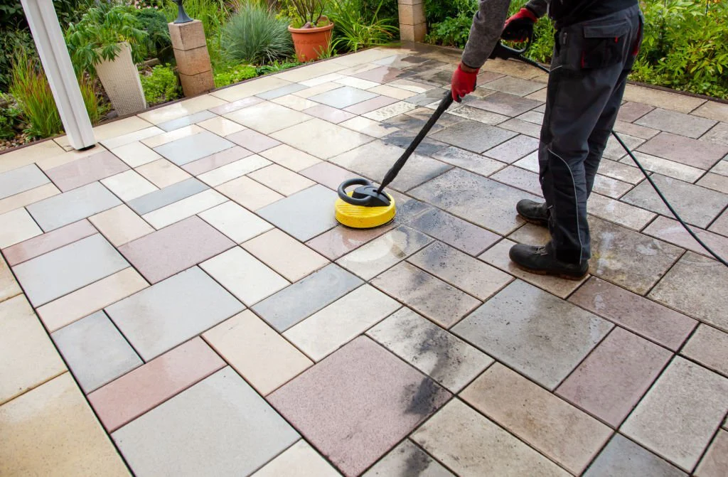 Professional floor cleaning technician using a pressure-washing surface cleaner to restore outdoor stone patio tiles, removing dirt and grime